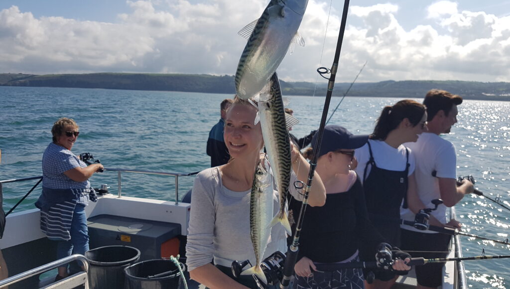 Epic Fishing 1 On a family-friendly fishing trip, passengers reel in mackerel off New Quay, Wales, with Cardigan Bay sparkling in the background.
